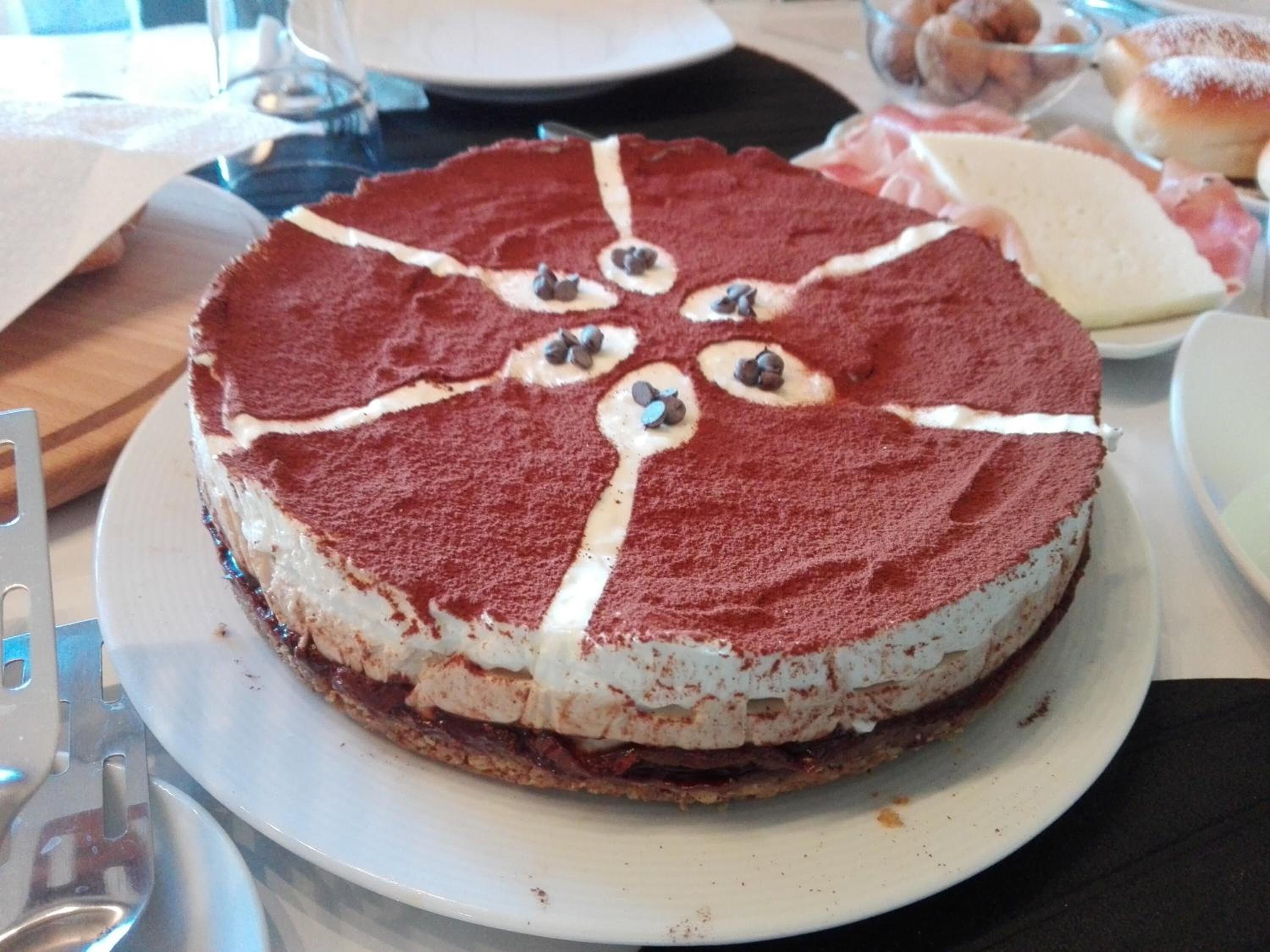 Pastís rodó amb crema blanca i xocolates sobre un plat blanc.