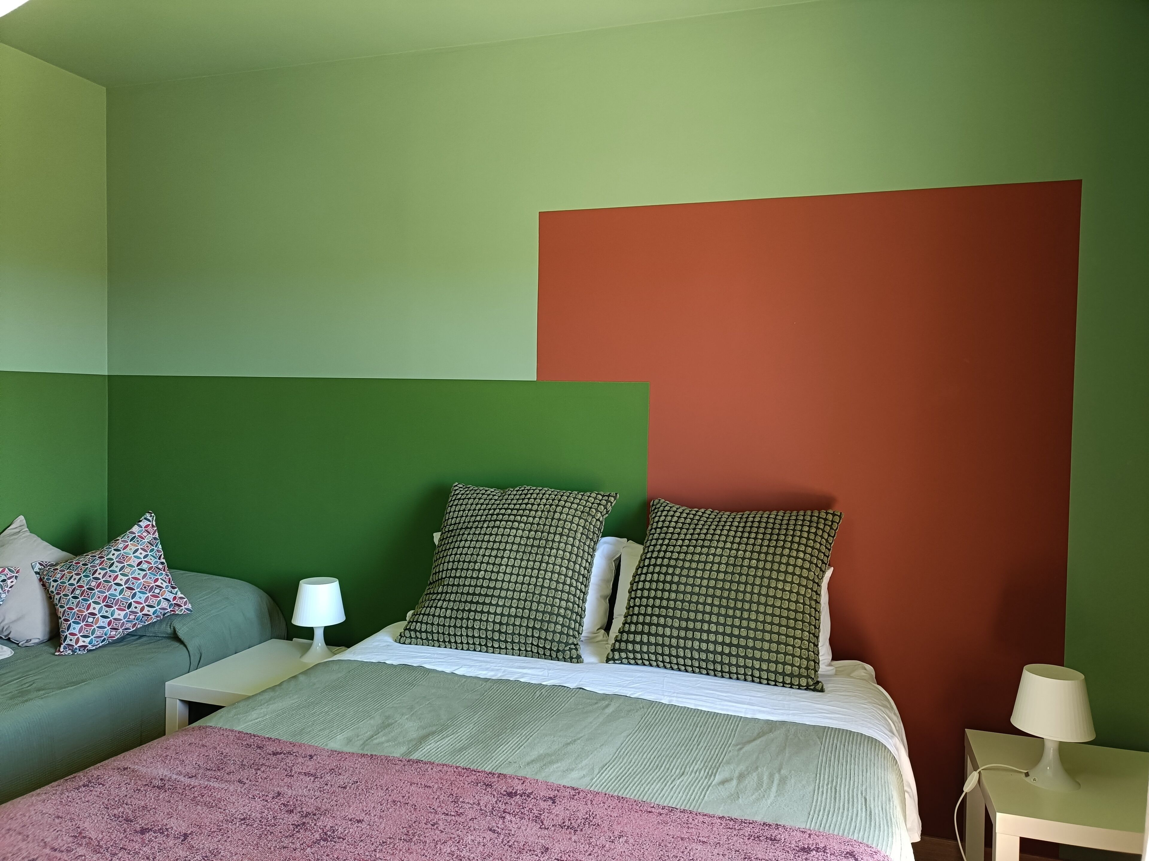 Um quarto com uma cama, uma mesinha de cabeceira, uma luminária e um sofá com almofadas.