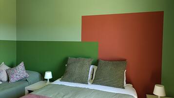 Um quarto com uma cama, uma mesinha de cabeceira, uma luminária e um sofá com almofadas.