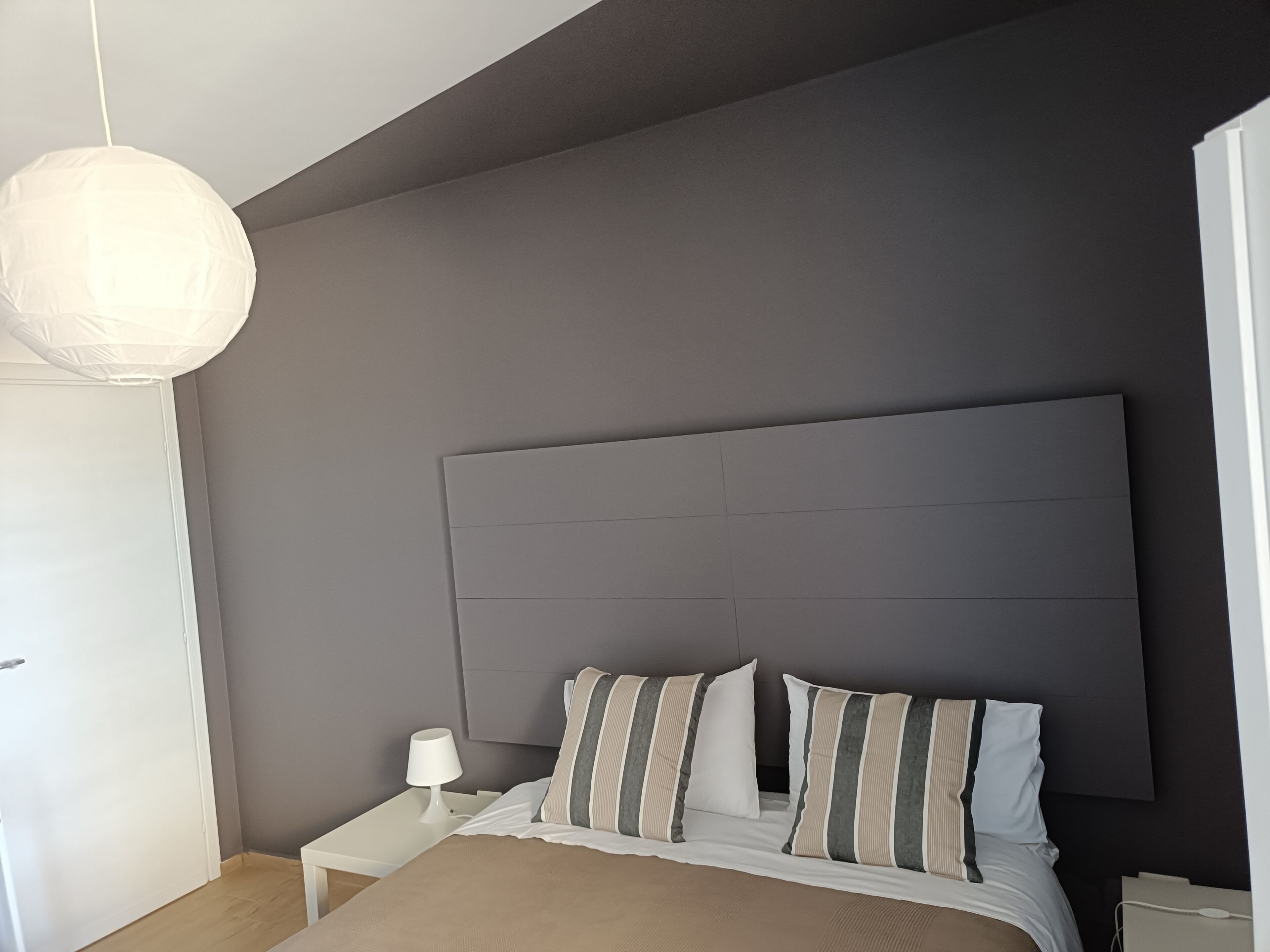 A bedroom with a bed, bedside table, lamp, and a hanging light fixture.