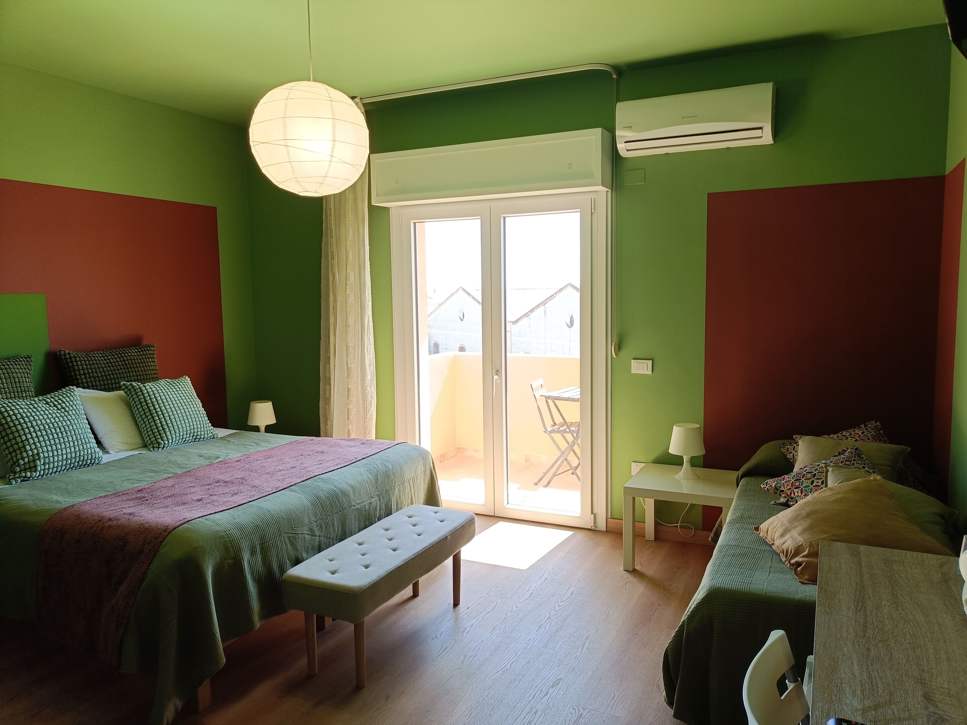 A room with a bed, bench, table, and a view through a door.