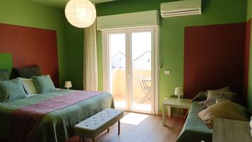 A room with a bed, bench, table, and a view through a door.