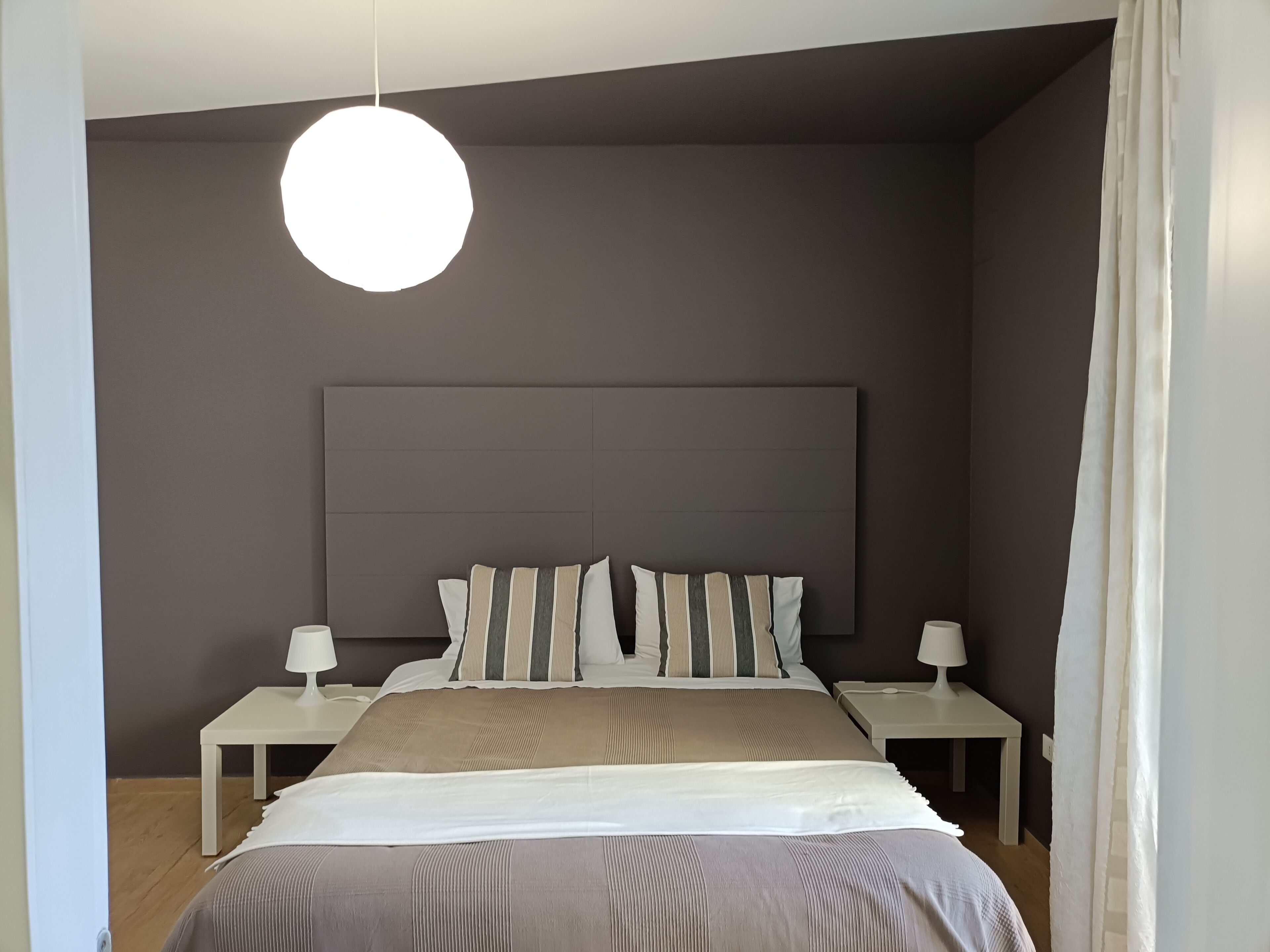 Une chambre à coucher moderne avec un grand lit, deux tables de chevet, un luminaire suspendu et une tête de lit de couleur foncée.