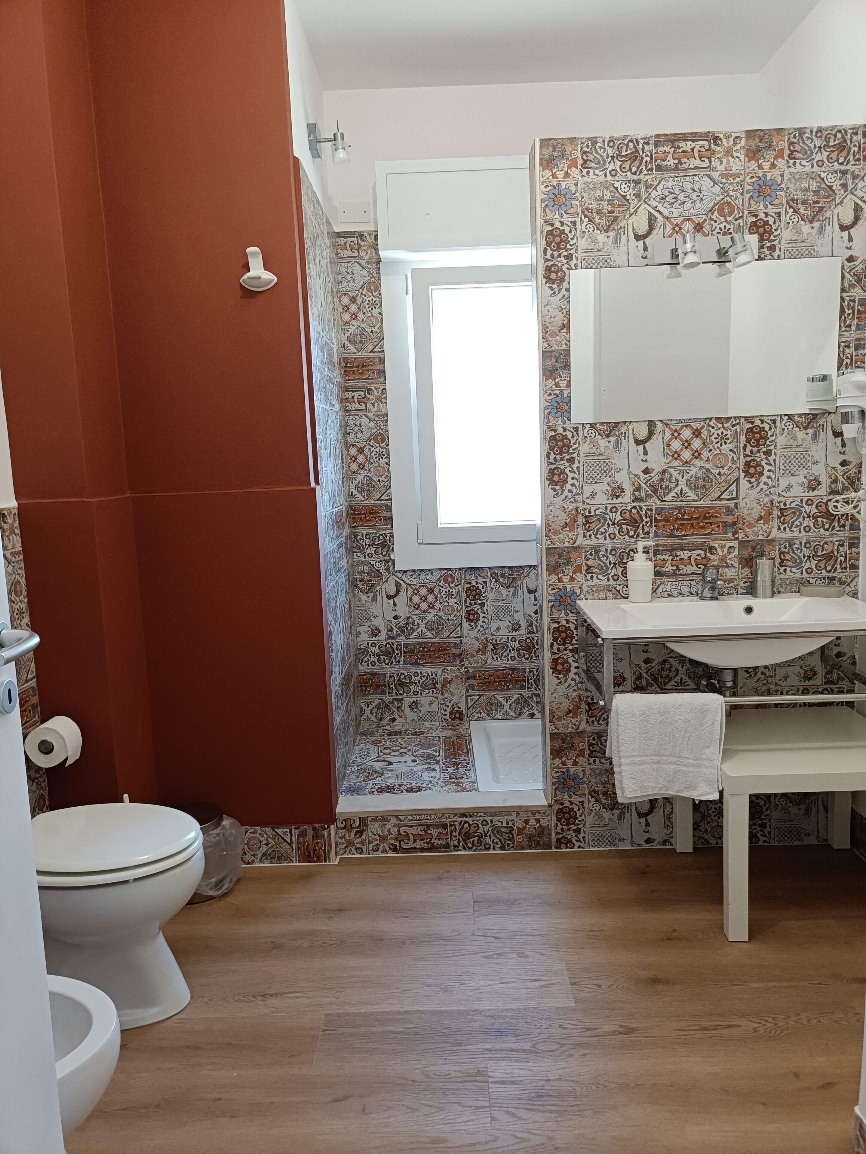 Une salle de bain avec des toilettes blanches, un lavabo avec un miroir et un espace douche.