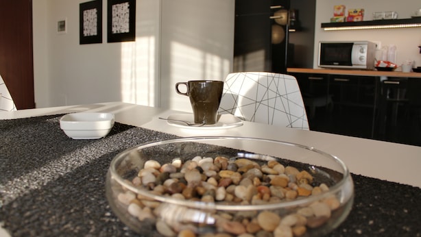 Un comedor con una mesa lista para dos, un tazón de nueces variadas, una taza y un microondas al fondo.