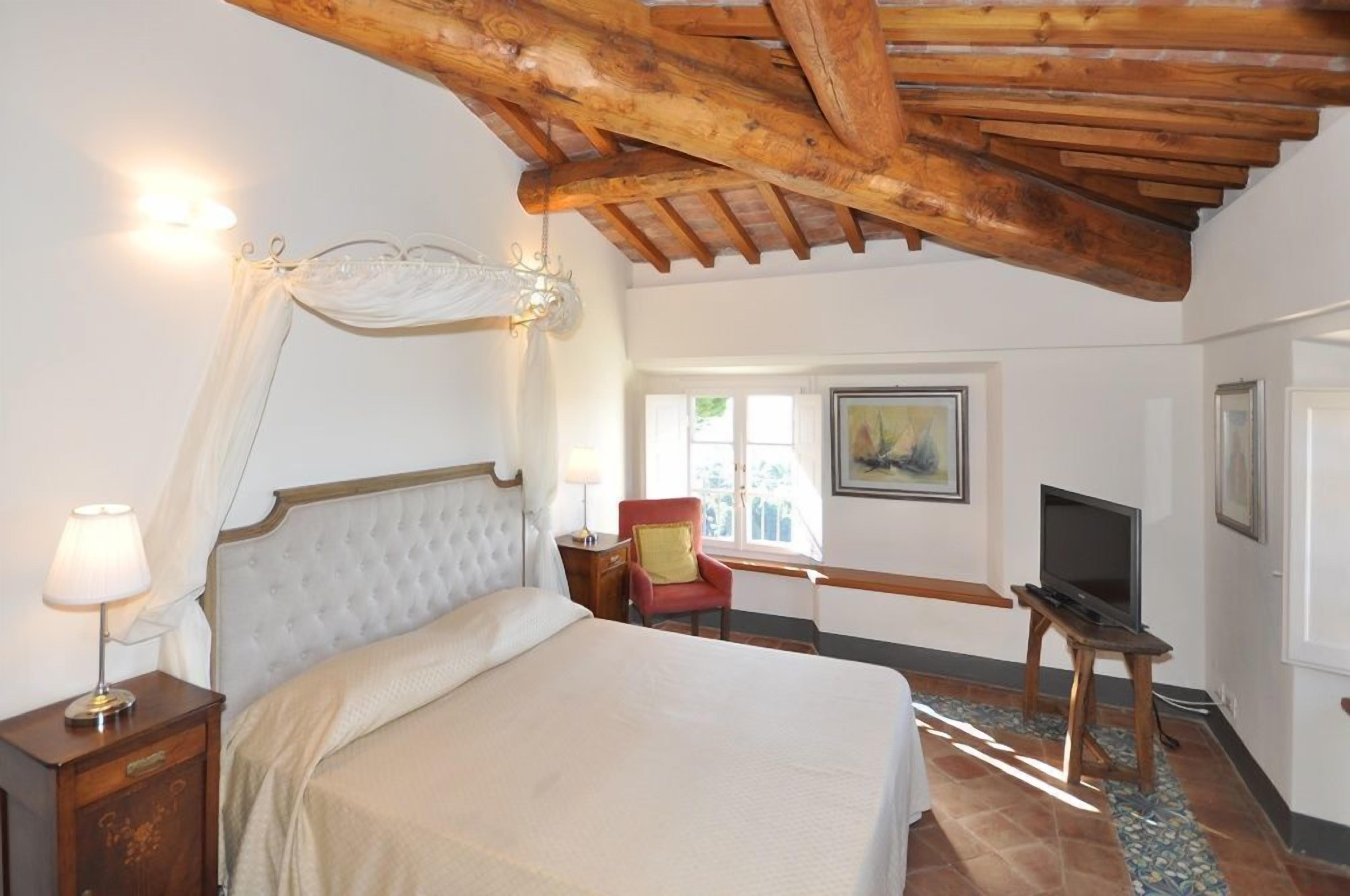 Een slaapkamer met een bed, een stoel, een televisie en een raam.