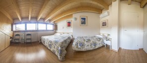 A room with wooden ceilings, two beds with floral bedding, a radiator, and a window with a view. - Piccolo Hotel Tanamalia (Lizzano in Belvedere)