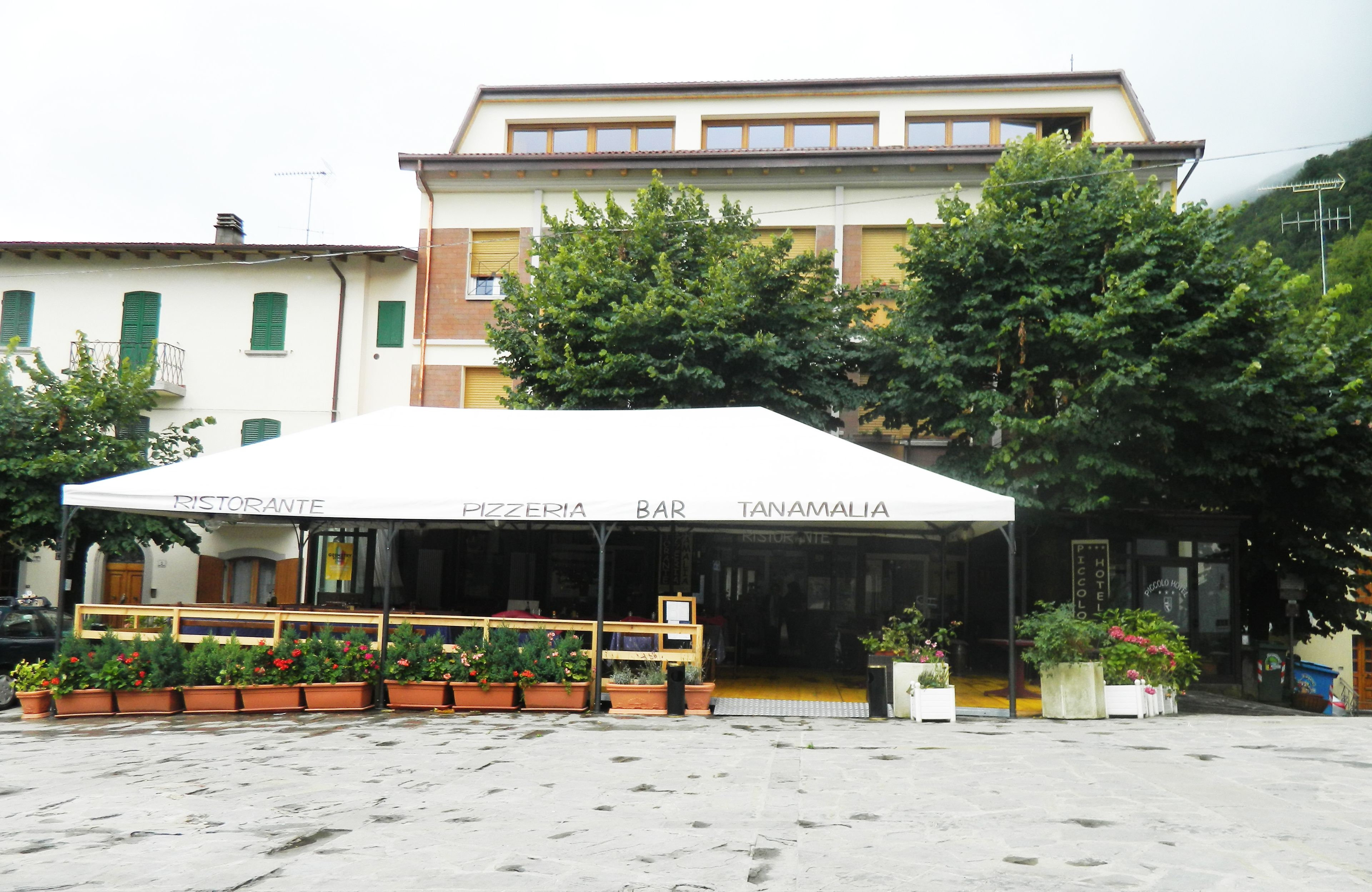 A restaurant with outdoor seating, a white awning, and potted plants.