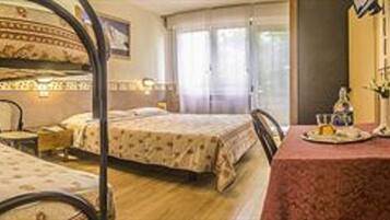 A hotel room with two beds, a dining table with a red tablecloth, and a window with curtains.