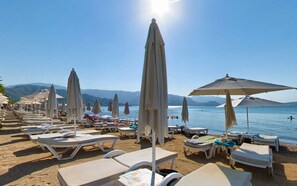 Une plage avec des transats et des parasols, un ciel dégagé et des montagnes en arrière-plan.