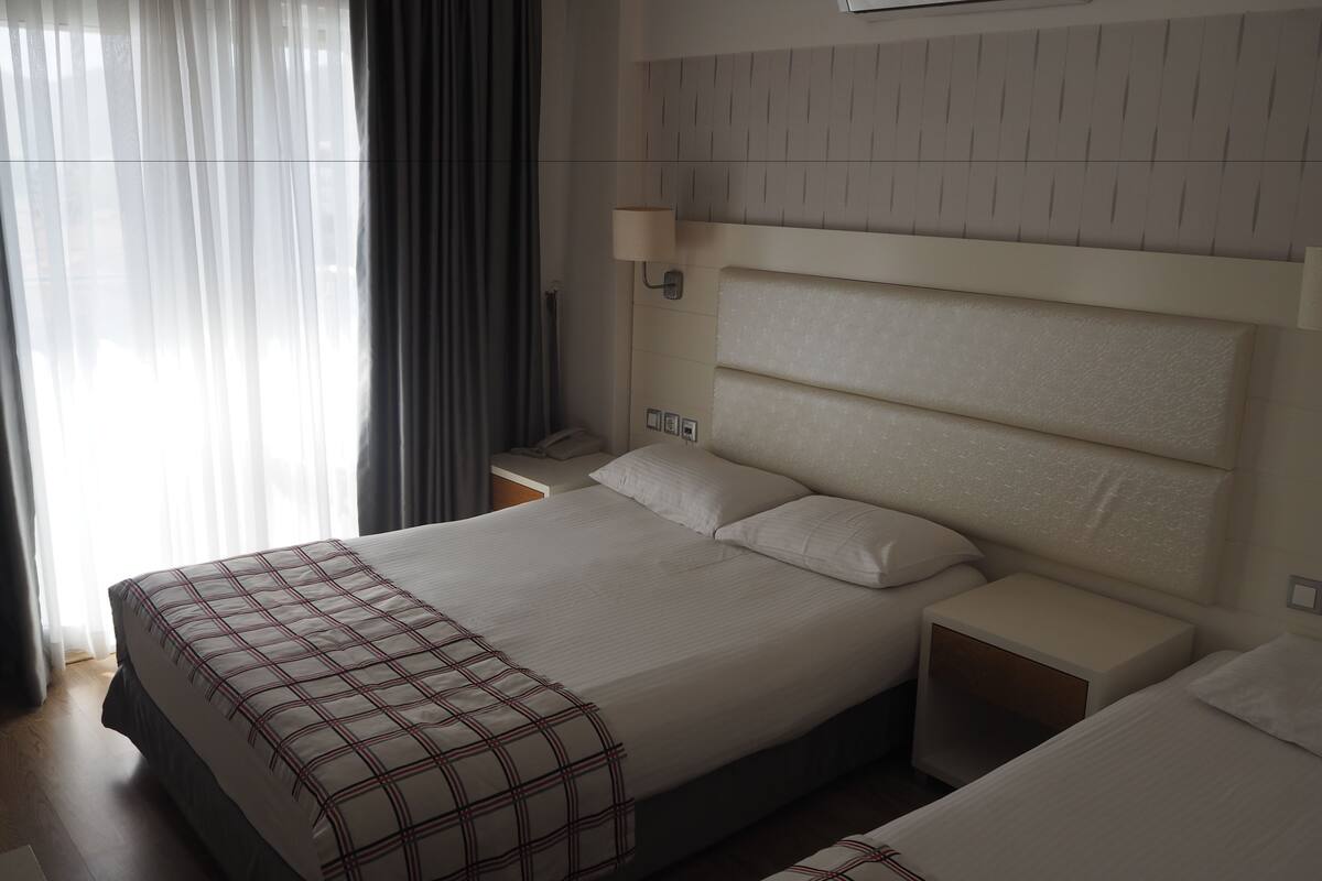 A hotel room with a large bed, bedside tables, a lamp, and a window with curtains.