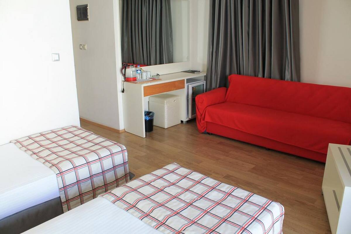 A hotel room with a red sofa, two beds with plaid bedding, a desk with a computer, and a large mirror.