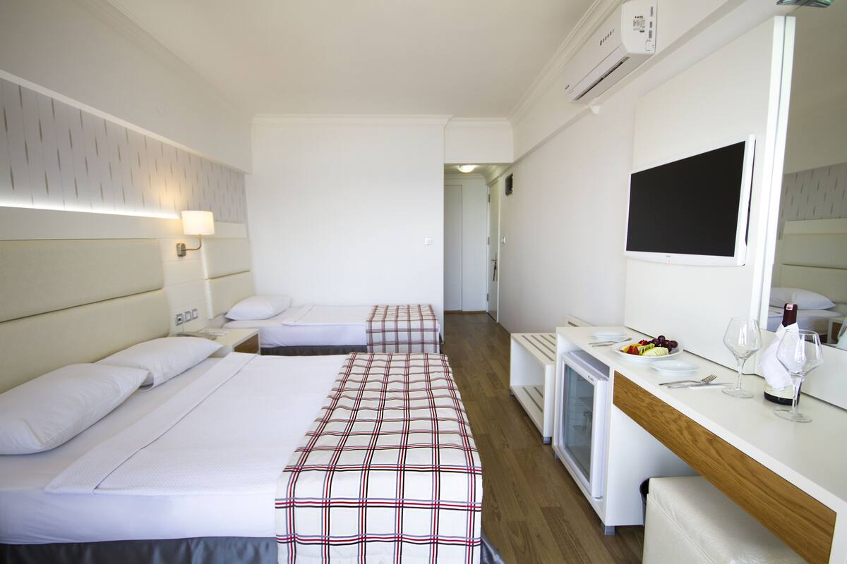 A hotel room with two beds, a desk with a mirror, a small kitchenette, and a TV.
