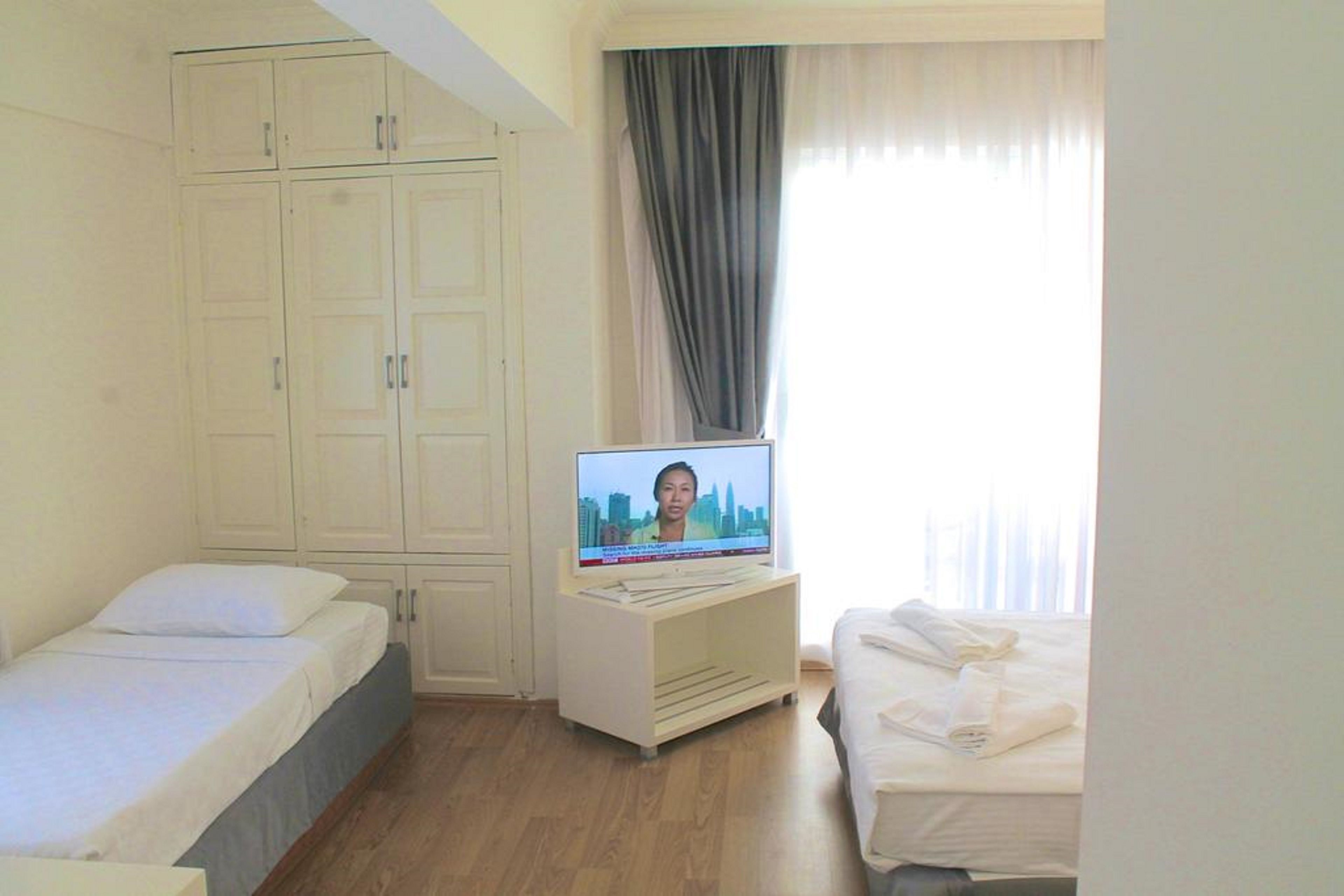 A hotel room with two beds, a television on a stand, a wardrobe, and a window with curtains.