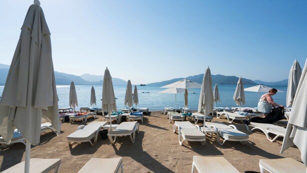 A beach with sun loungers and umbrellas, a clear sky, and mountains in the background. - Yunus Beach Hotel (Marmaris)