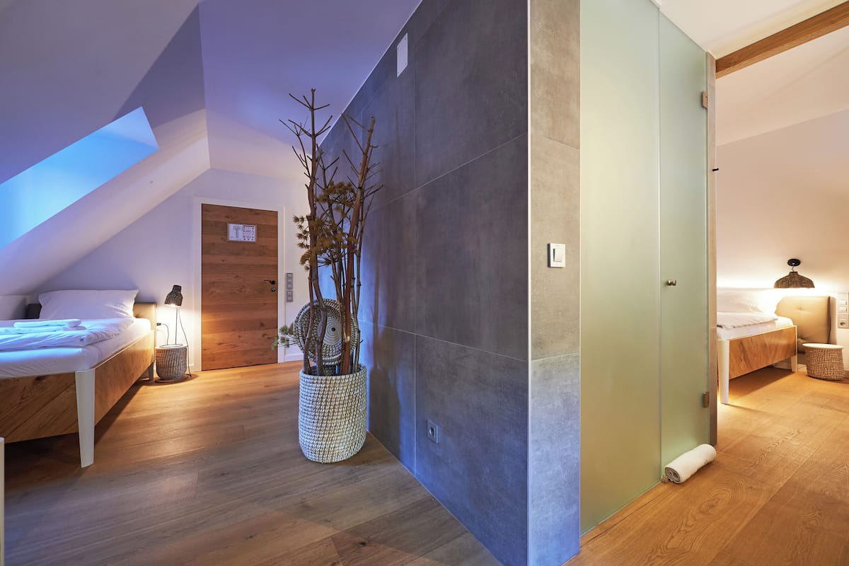 A modern hotel room with a sloped ceiling, a large potted plant, and a bed with a wooden headboard.