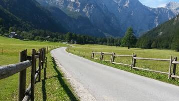 A rural road with a wooden fence on one side and a mountain range in the background.