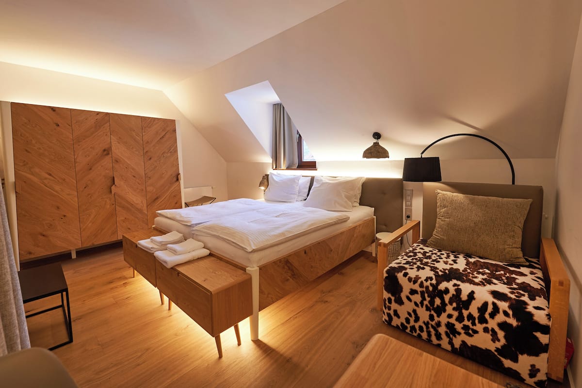 A modern bedroom with a loft-style bed, a daybed, a wooden wardrobe, and a skylight.