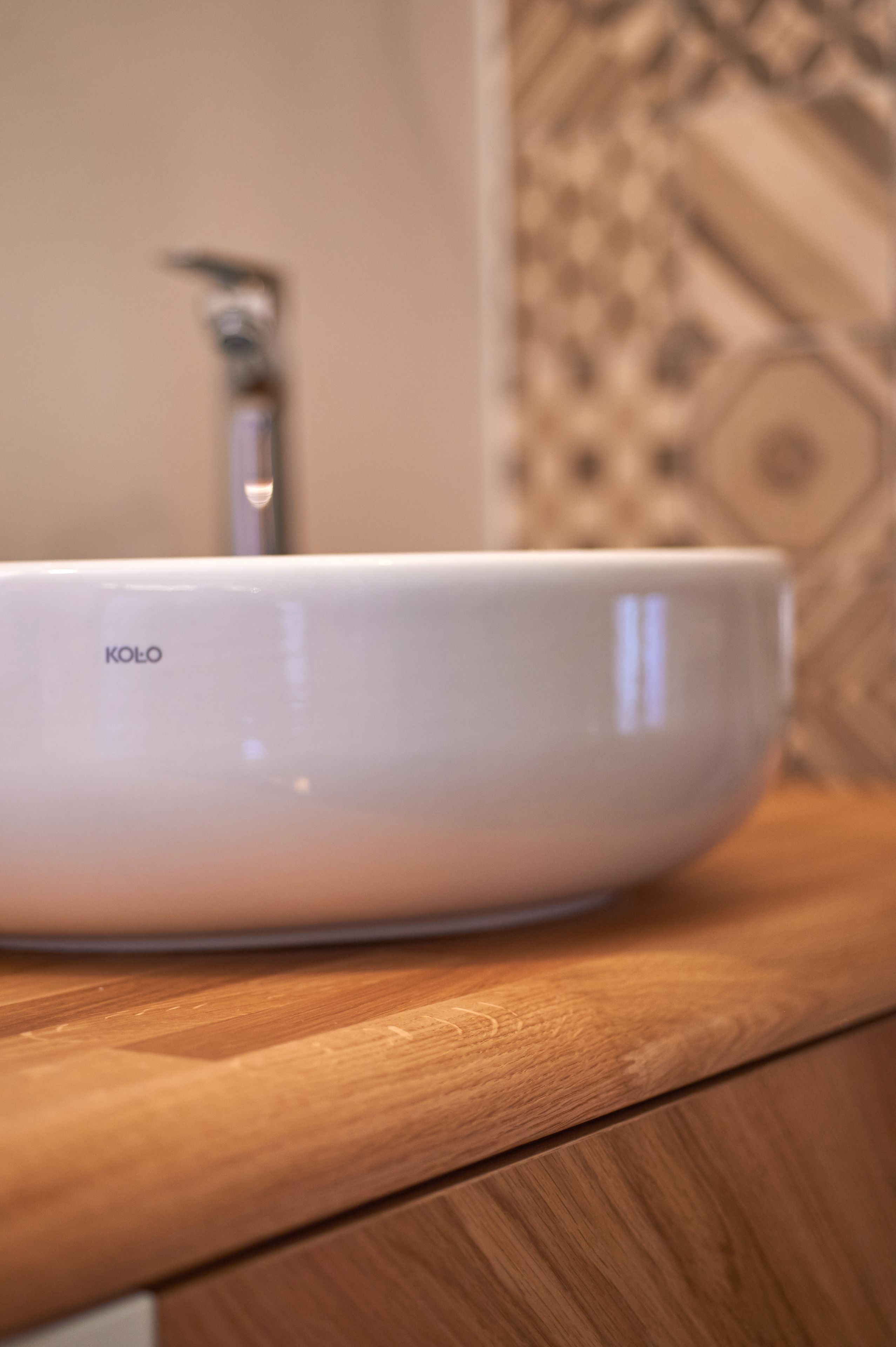 A white Kolo bowl on a wooden countertop.