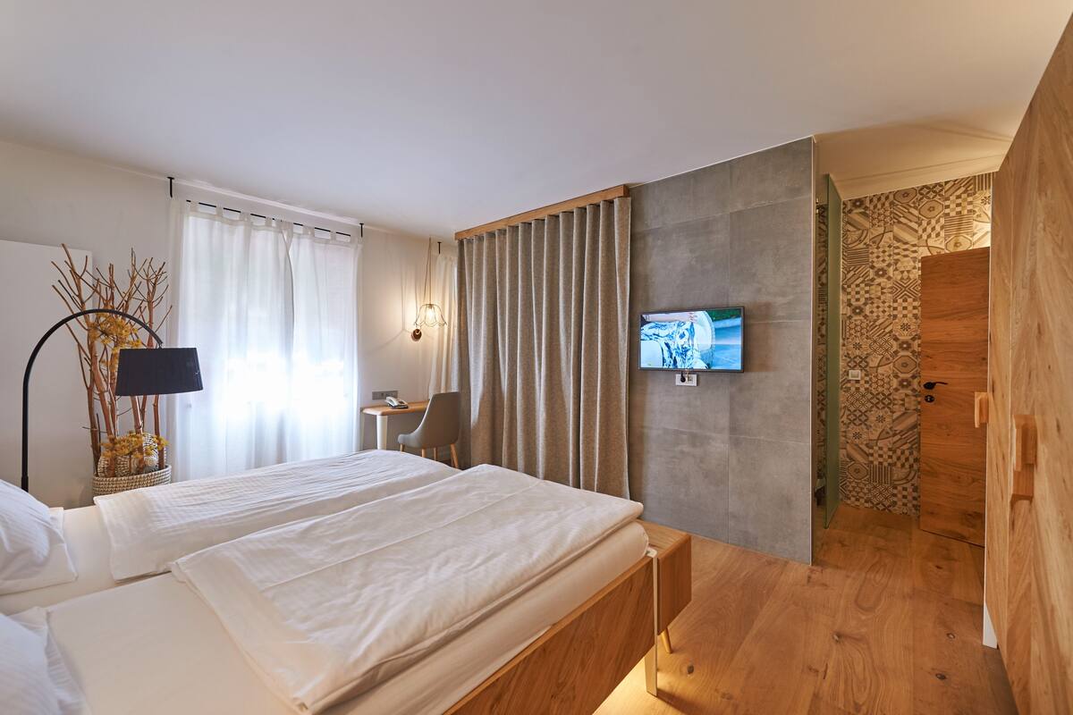 A modern hotel room with a bed, a desk, a television, and a view of a patterned wall and wooden door.