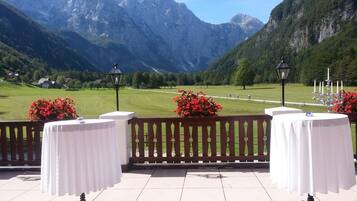 A terrace with tables set for dining, overlooking a mountainous landscape.