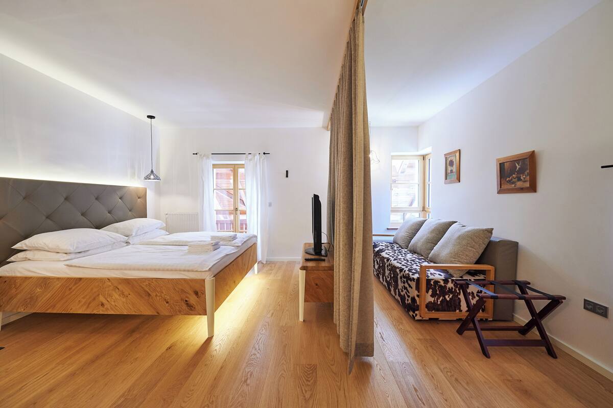 A modern bedroom with a wooden bed, a sofa, and a TV.