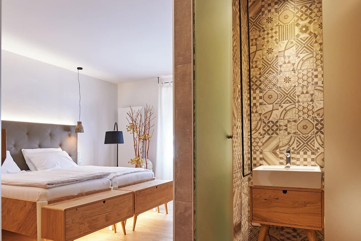 A modern bedroom with a bed, bedside table, and a bathroom with a sink and mirror.