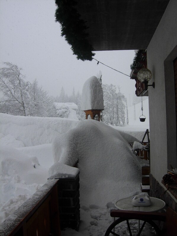 A snow-covered outdoor area with a wooden bench and a chair, a snow-covered statue, and a building with a porch. - Hotel Albe (Rocca Pietore)