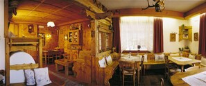 A cozy wooden room with a dining area, a sofa, and a window with curtains. - Hotel Albe (Rocca Pietore)