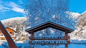A wooden sign for Ristorante Hotel La Pesaia with a stone wall base, surrounded by snow-covered trees and mountains in the background. - Hotel La Perla (Ravascletto)