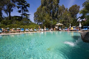 Una piscina cristalina rodeada de sillas de descanso y sombrillas, con árboles al fondo.