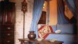 Een slaapkamer met hemelbed, een houten dressoir, een tafel met een vaas en een wandlamp.