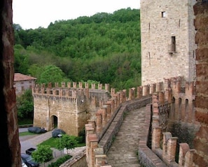 A historic stone wall with a narrow pathway leading to a tower. - Castello di Vigoleno (Vernasca)