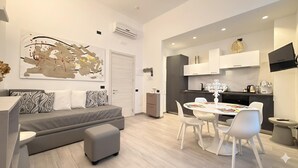 A modern living room with a grey sofa, a coffee table, and a dining area with a white table and chairs. - Hotel Europa (Varese)