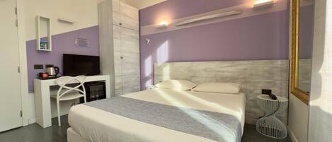 A modern hotel room with a large bed, a TV, a desk, and a wardrobe.