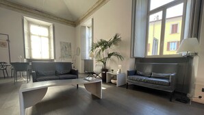 A spacious living room with a modern design, featuring a grey sofa, a coffee table, and a potted plant. - Hotel Europa (Varese)