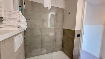 A modern bathroom with a glass-enclosed shower, a white sink, and a towel rack with folded towels.