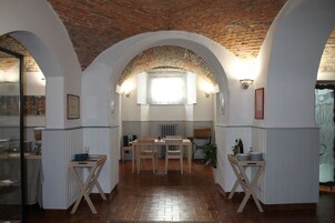 Un comedor con techo de ladrillo, paredes blancas y suelo de ladrillo. Hay una mesa con sillas y una mesa pequeña con platos y botellas.