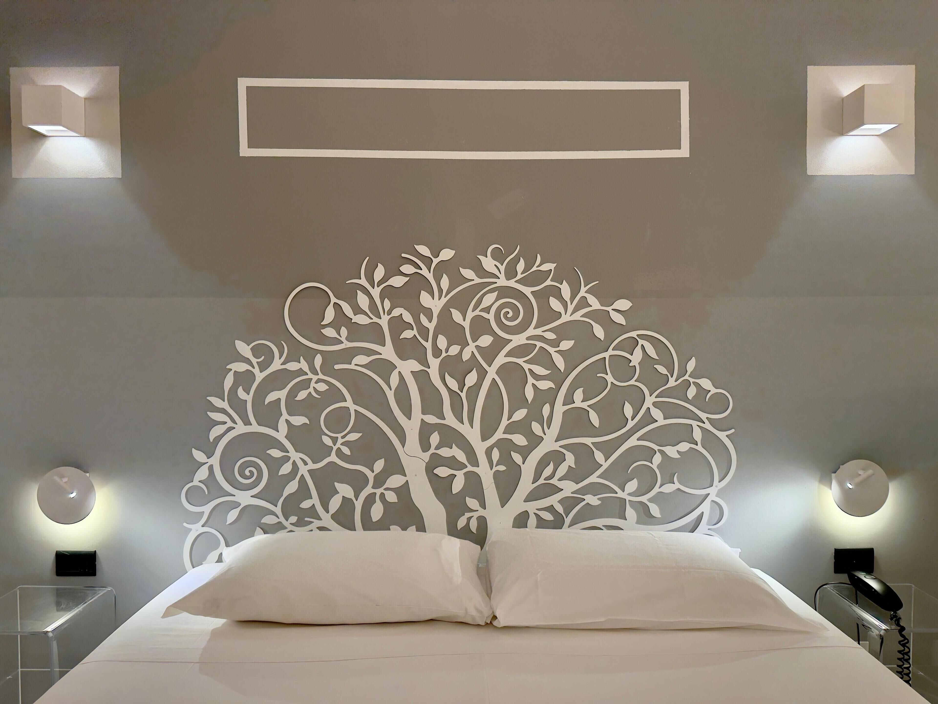 Un dormitorio con un cabecero decorativo, una cama con ropa de cama blanca, dos lámparas de noche y un aplique en la pared.