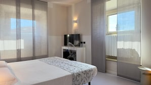 A modern hotel room with a large bed, a flat-screen TV, a small seating area, and large windows with sheer curtains. - Hotel Europa (Varese)