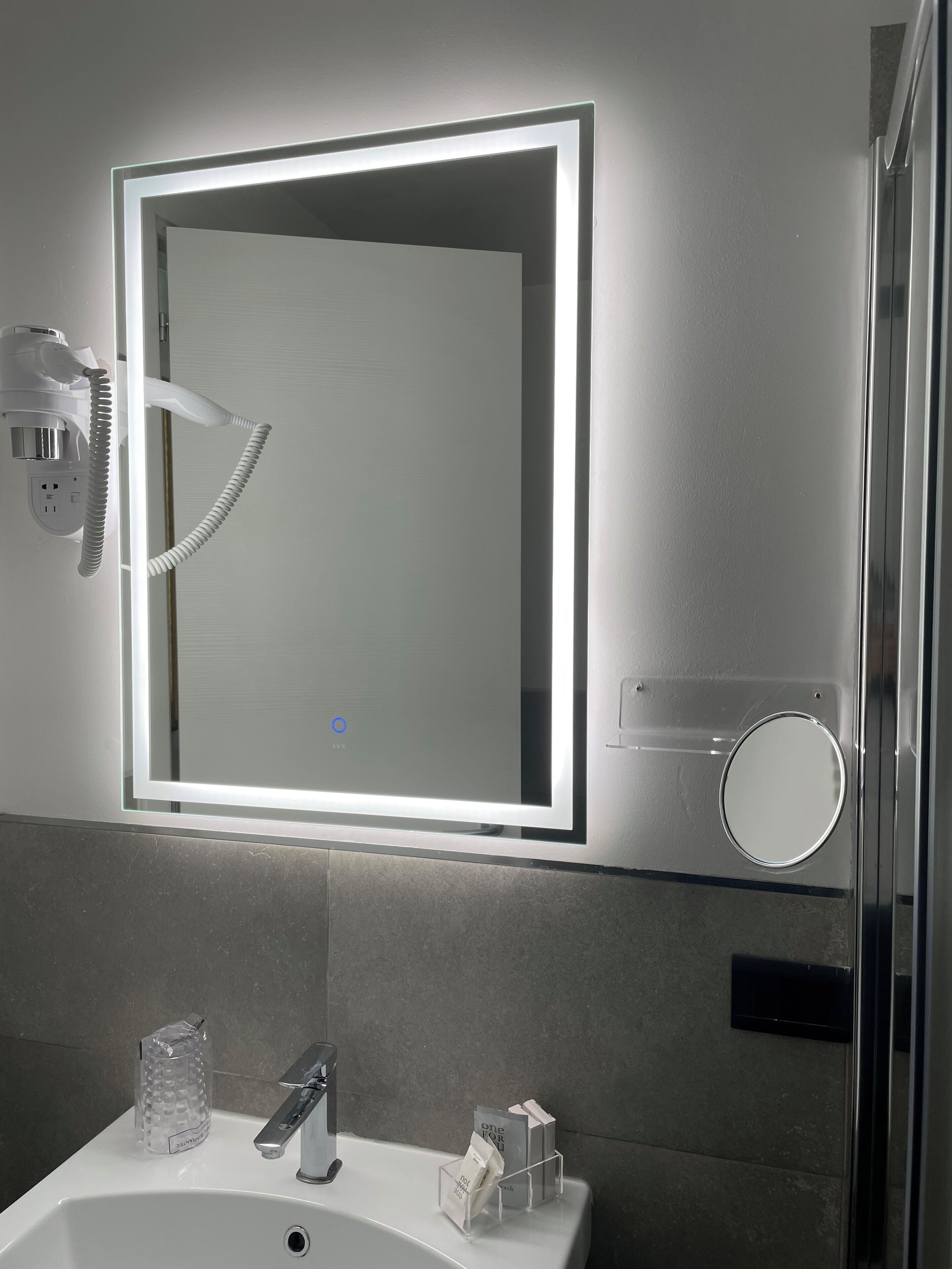 A bathroom with a mirror, a hairdryer, a sink, and a glass of water.