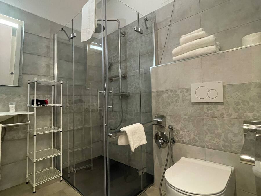 Un baño moderno con cabina de ducha de vidrio, inodoro blanco y estantería metálica.
