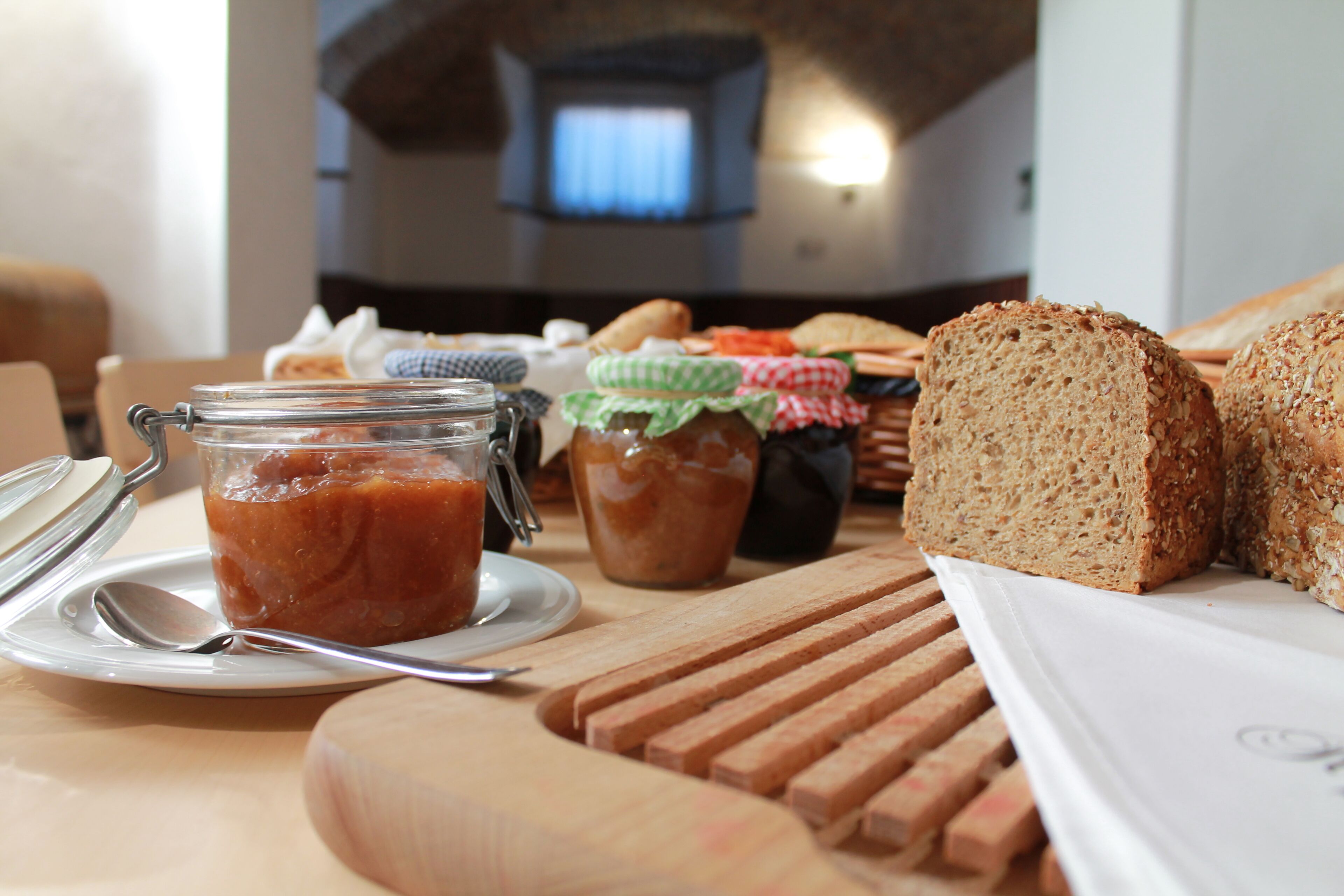 Una mesa con pan, frascos de mermelada y una tabla de cortar.