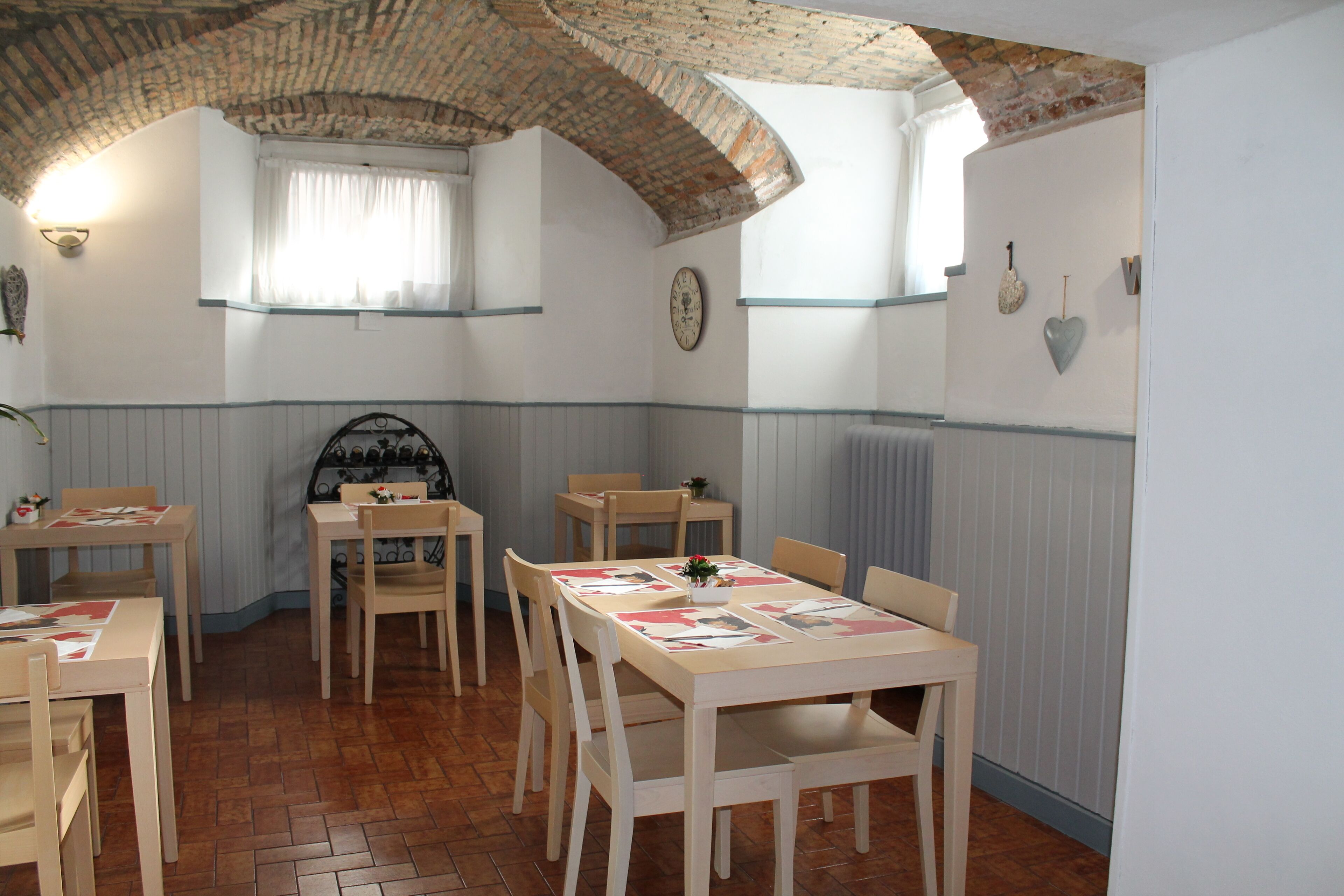 Un comedor con mesas y sillas de madera, techo de ladrillo y ventana con cortinas.