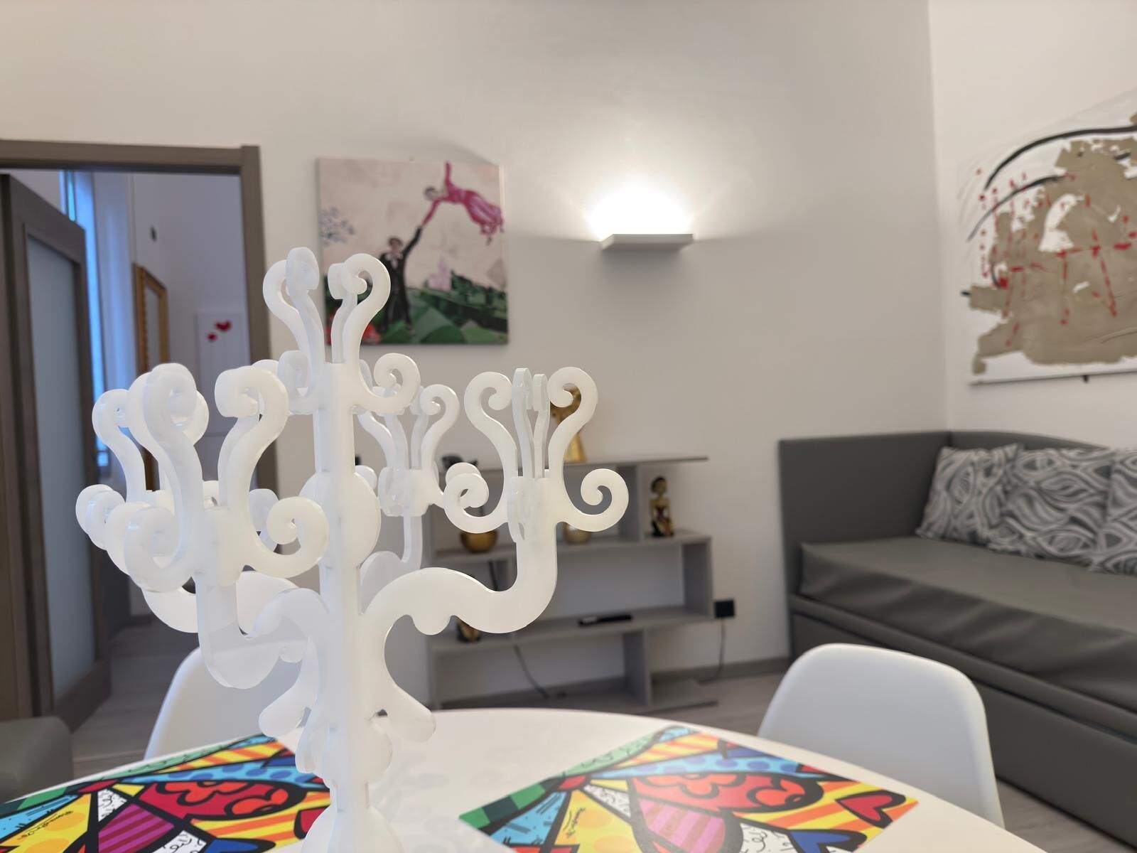 Una sala de estar moderna con un candelabro blanco sobre una mesa, un sofá gris y un mantel colorido.