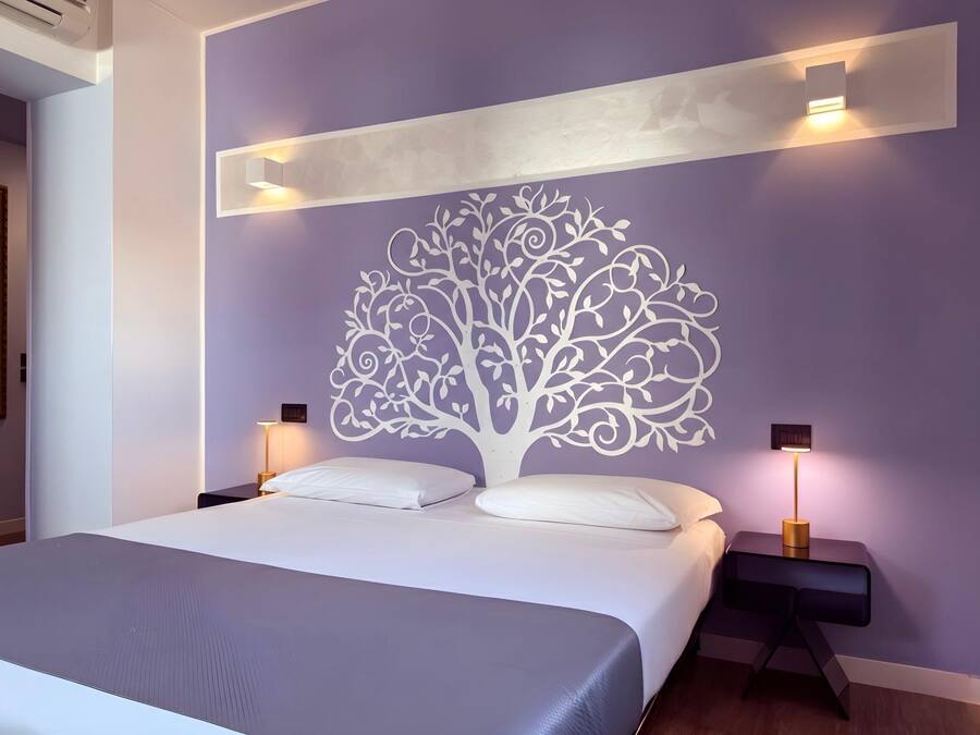 A modern bedroom with a large bed, two bedside tables, and a decorative tree mural on the wall.