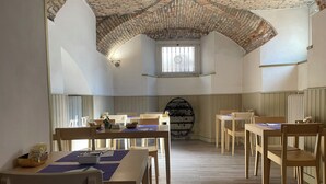 A dining area with wooden tables and chairs, a brick ceiling, and a window with bars. - Hotel Europa (Varese)
