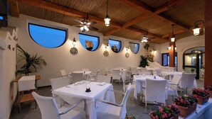 Un restaurant avec des tables recouvertes de nappes blanches, des chaises en osier et des plantes en pot.