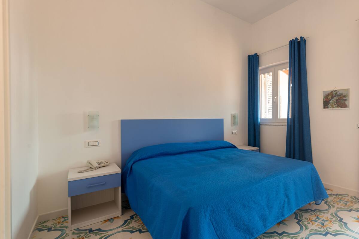 Ein Schlafzimmer mit einem Bett, einem Nachttisch, einem Telefon und einem Fenster mit Vorhängen.