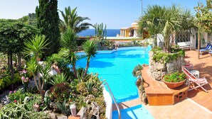 A pool surrounded by tropical plants and a view of the sea. - Hotel Villa Sirena (Serrara Fontana)